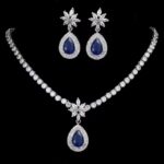 Elegant sapphire and crystal teardrop necklace and earring set with floral accents on black background